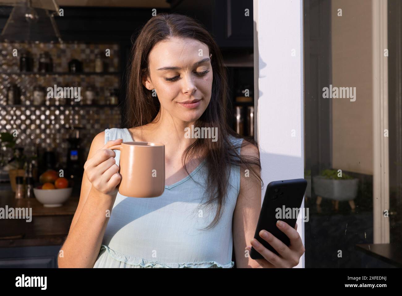 Smartphone-Nachricht liest, Frau, die Kaffeetasse in der Küche hält Stockfoto