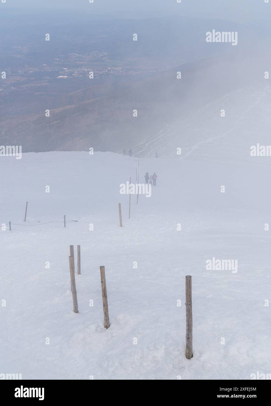 Bergpfad mit hohen Säulen und Silhouetten von Touristen an einem sehr nebligen, schneebedeckten Wintertag. Krkonosze (Riesengebirge), Sniezka, Polen Stockfoto