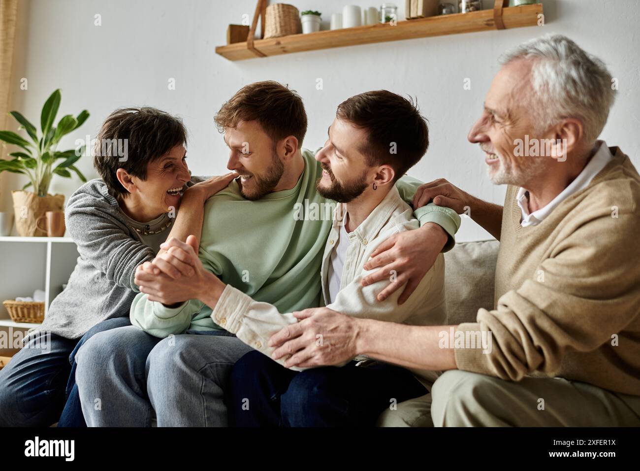 Ein schwules Paar sitzt auf einer Couch mit Eltern, lacht und umarmt. Stockfoto