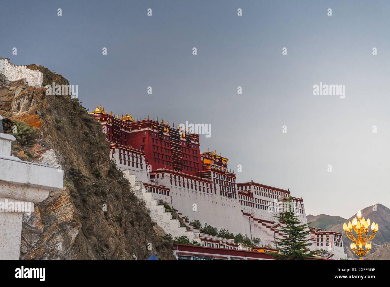 Die abgewinkelte Front des Potala-Palastes wurde oben und die Straßenlandschaft unten unter einem klaren blauen Himmel während des frühen Abends in Lhasa, Tibet, angehoben. Horizontal Stockfoto