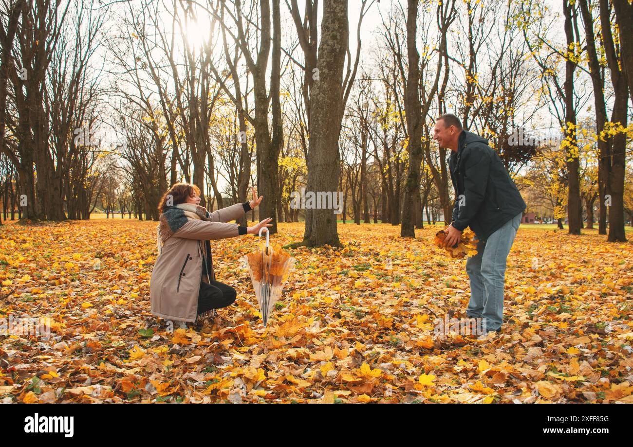Ein verheiratetes Paar über 50 Jahre alt, spaziert im Herbst an einem warmen sonnigen Tag durch den Park, spielt mit fallenden Blättern und lacht, verbringt einen freien Tag Stockfoto