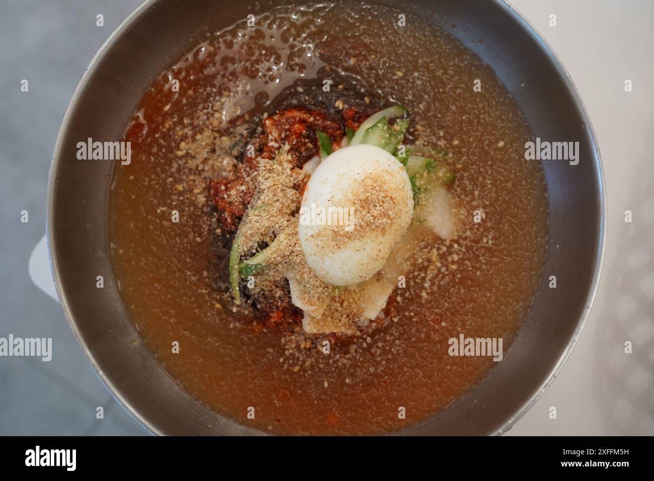 Naengmyeon ist ein einzigartiges koreanisches Nudelgericht, das aus kalter Brühe mit Gewürzen und Belägen zubereitet wird Stockfoto