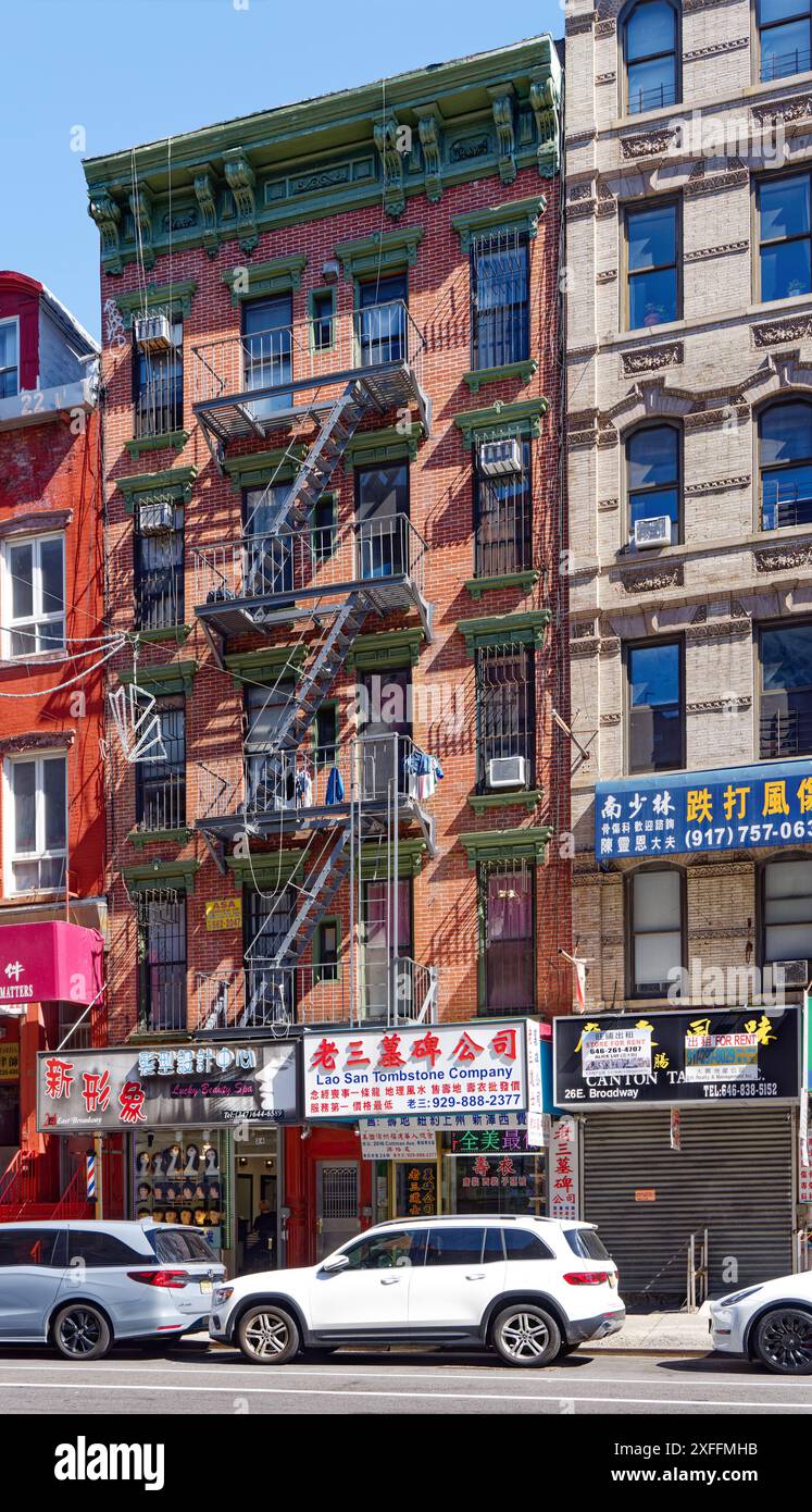 NYC Chinatown: 24 East Broadway ist ein fünfstöckiges Wohnhaus aus rotem Backstein über Straßenläden mit grünen Fensterleisten und Metallgesims. Stockfoto