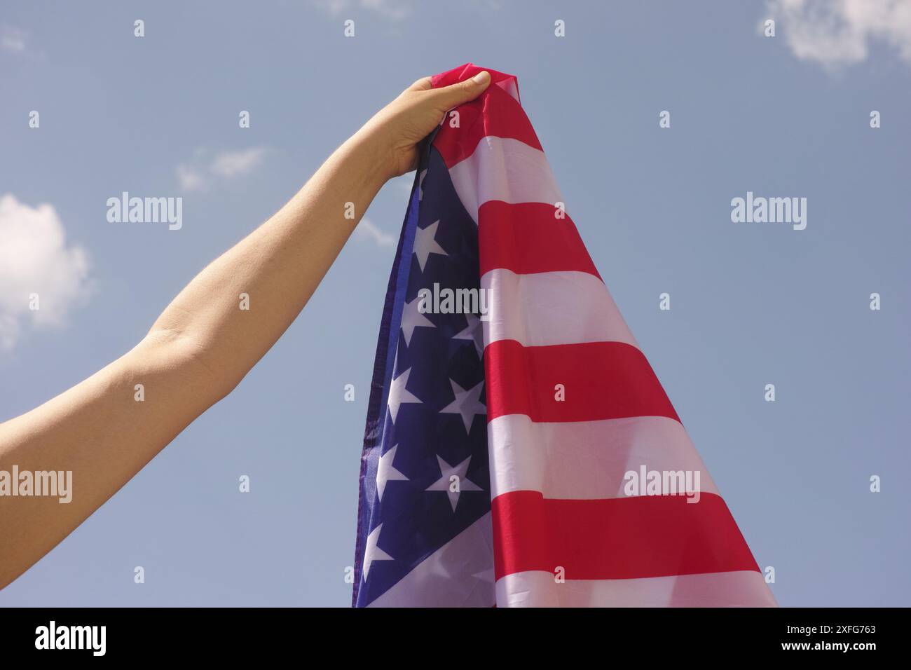 Eine Frau, die eine amerikanische Flagge in der Hand vor einem blauen Himmel hält. Stockfoto