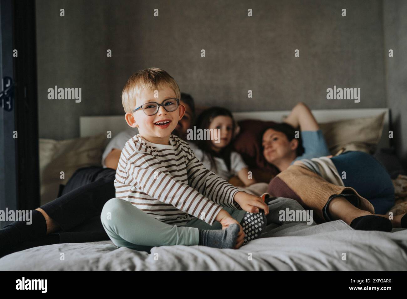 Porträt eines niedlichen Jungen, der mit Familie zu Hause auf dem Bett sitzt Stockfoto