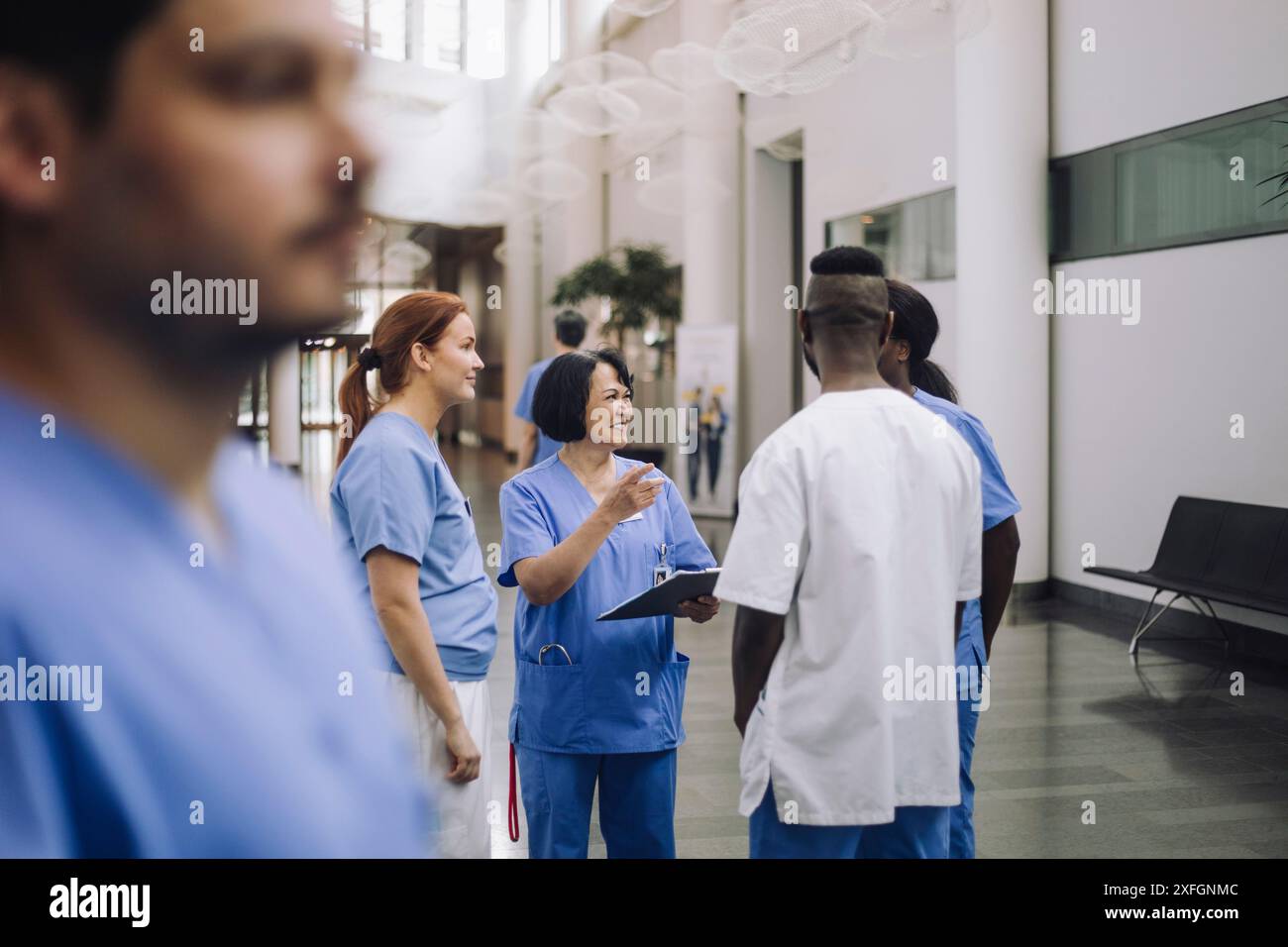 Lächelnder Seniorarzt, der mit medizinischem Personal spricht, während er in der Lobby des Krankenhauses steht Stockfoto