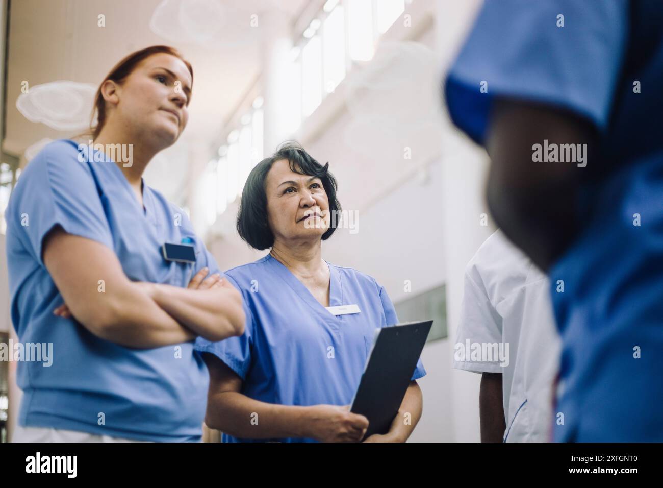 Weibliches medizinisches Personal hört Kollegen beim Stehen im Krankenhaus zu Stockfoto