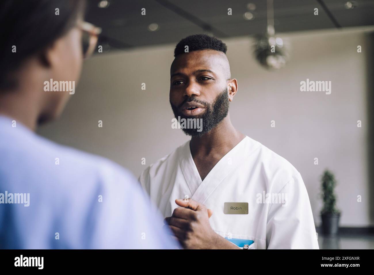 Bärtiger männlicher Arzt, der mit weiblichem Personal im Krankenhaus diskutiert Stockfoto