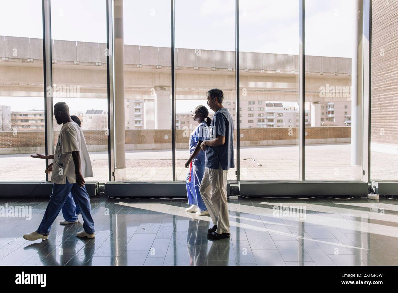 Männliche und weibliche Angehörige des Gesundheitswesens gehen in der Nähe von Glasfenstern im Büro Stockfoto