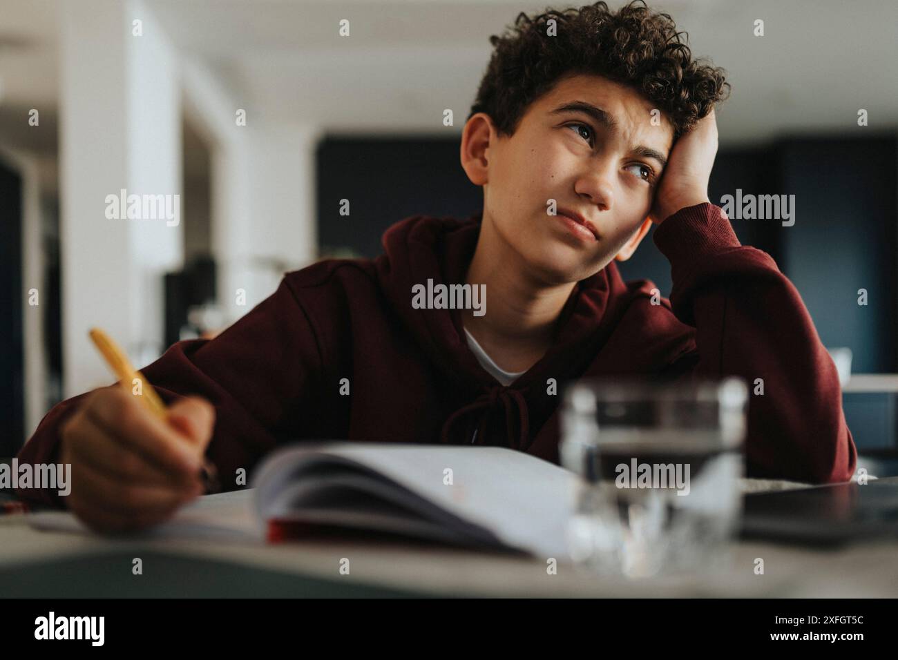 Verwirrter Junge mit Kopf in Hand, der zu Hause studiert Stockfoto