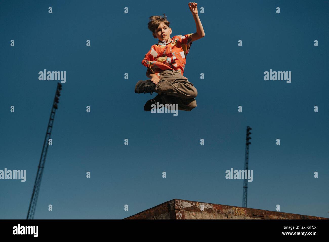 Junge, der mitten in der Luft gegen den blauen Himmel springt Stockfoto