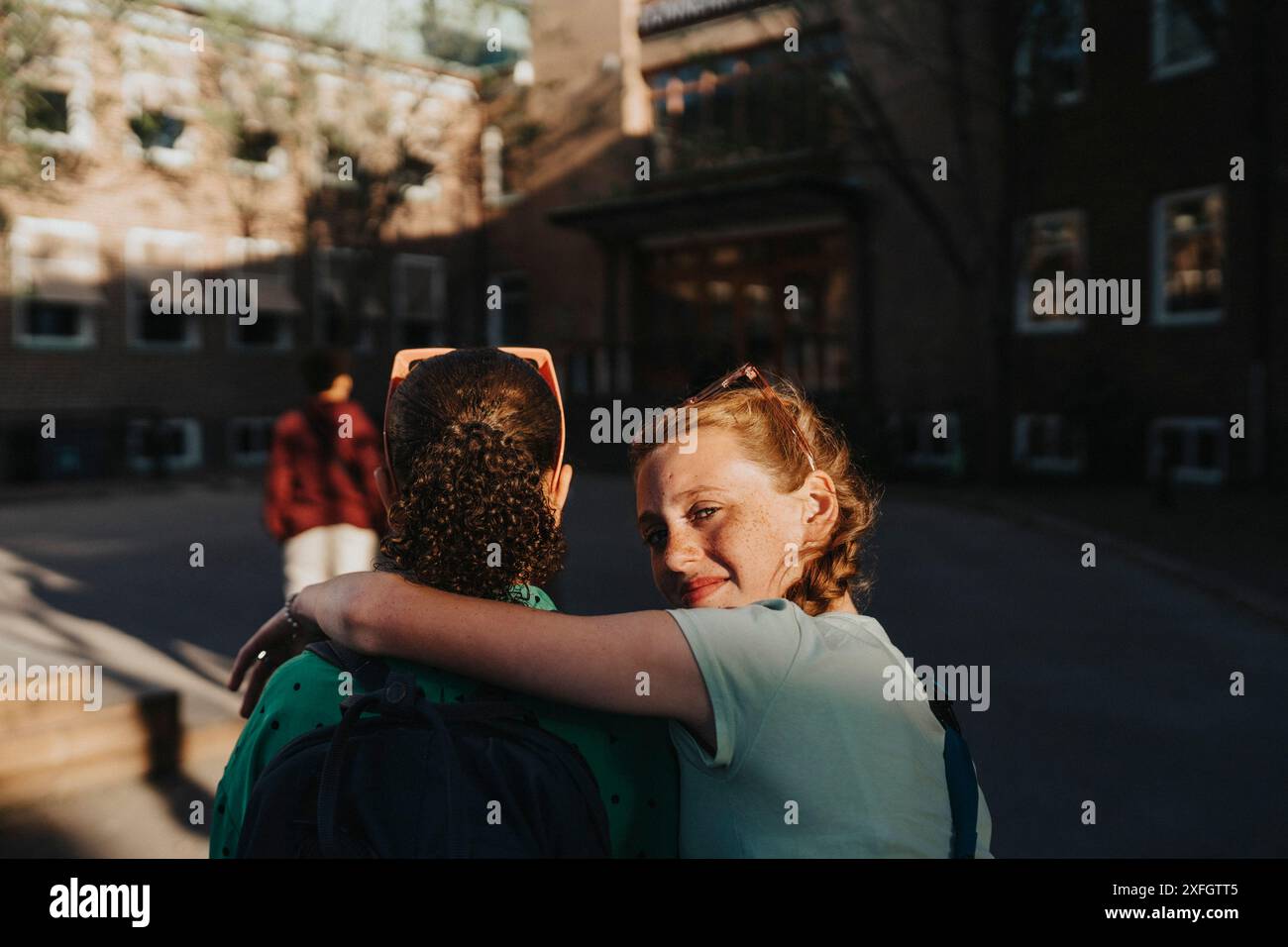 Porträt eines lächelnden Mädchens mit einem Arm um einen Freund, der über die Schulter schaut, während er auf dem Schulgelände läuft Stockfoto
