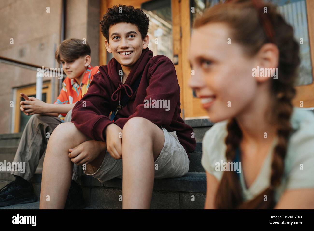 Lächelnder Junge, der mit Freunden auf der Treppe des Schulgebäudes sitzt Stockfoto