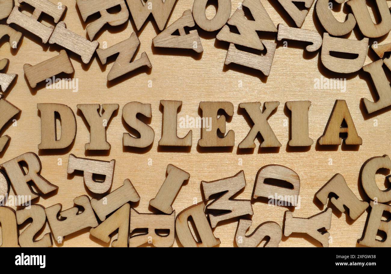 Legasthenie, Wort in hölzernen Alphabeten umgeben von zufälligen Buchstaben auf hölzernem Hintergrund Stockfoto