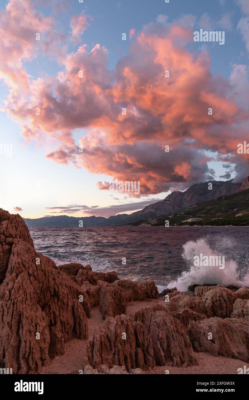 Farbenfroher Sonnenuntergang auf dem Meer. Rot-orange Wolken, Wellen brechen gegen die Felsen, gefärbt von der untergehenden Sonne. Die Küste Kroatiens. Stockfoto