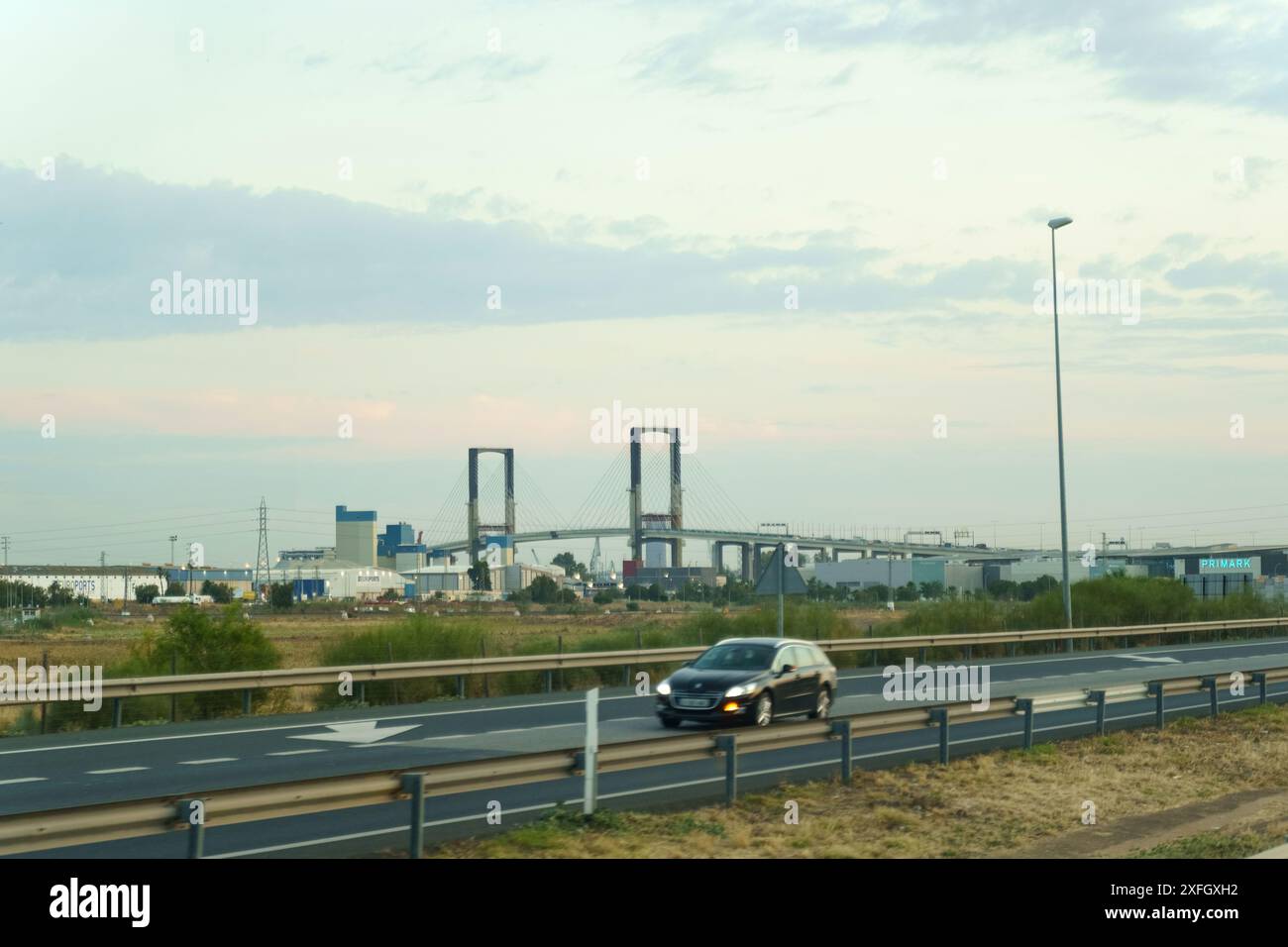 Sevilla, Spanien - 2. Juni 2023: Ein schwarzer Wagen fährt über eine Autobahn in Richtung Puente de la Barqueta Brücke in Sevilla. Die untergehende Sonne wirft ein W Stockfoto