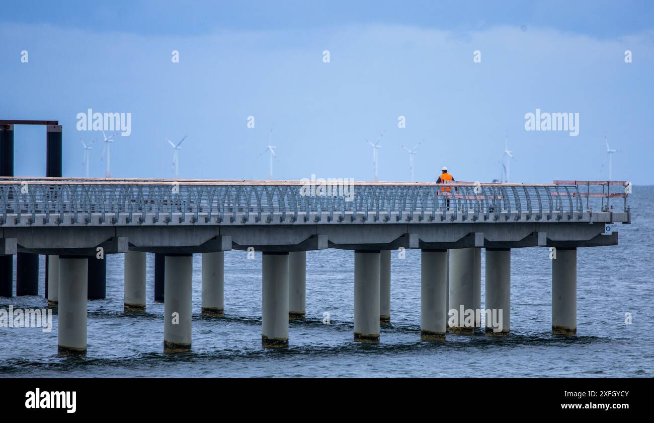 Prerow, Deutschland. Juli 2024. Ein Bauarbeiter überquert den Pier zum zukünftigen Inselhafen in der Ostsee. Der Inselhafen wird den Nothafen auf der Halbinsel Fischland-Darß-Zingst ersetzen. Der Bau der vor zwei Jahren begonnenen künstlichen Insel und der 720 Meter langen Pier, der längste im Ostseeraum, wird rund 42 Millionen Euro Kosten und in wenigen Wochen in Betrieb gehen. Der Inselhafen hat eine tropfenförmige Form, die bereits aus der Luft deutlich sichtbar ist. Quelle: Jens Büttner/dpa/Alamy Live News Stockfoto