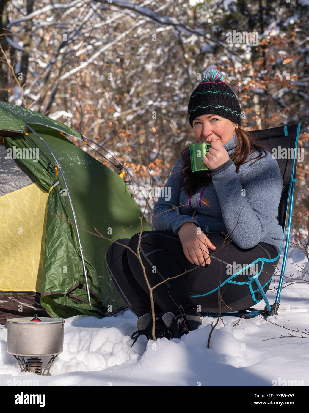 Eine Frau in der Nähe des Zeltes trinkt Tee. Wickelt das Seil auf. Nacht im Winterwald. Liebe für die Natur. Ökotourismus. Sonne, Wald, Schnee. Aktiver Lebensstil. T Stockfoto