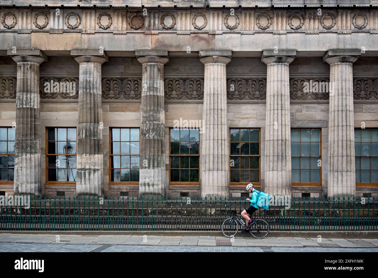 Deliveroo Essenskurier macht eine Pause an der Seite des Gebäudes der Royal Scottish Academy auf dem Hügel, Edinburgh, Schottland, Großbritannien. Stockfoto