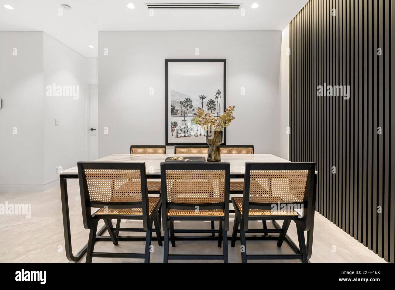 Ein moderner Speisesaal mit minimalistischem Design, Holztisch, Korbsessel und dekorativer Vase in einer gut beleuchteten Inneneinrichtung. Stockfoto