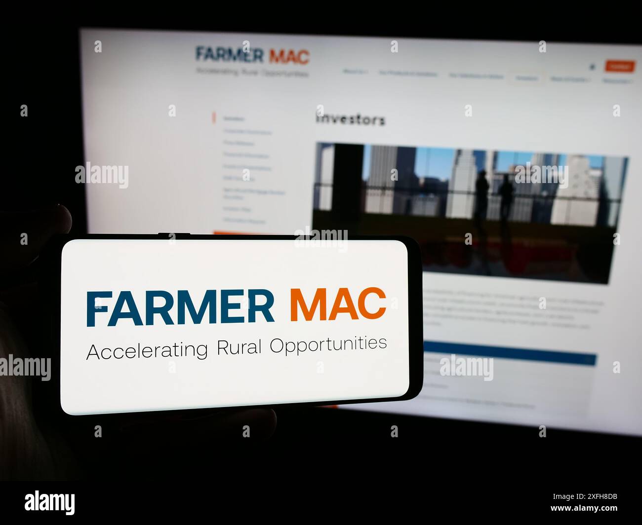 Person mit Smartphone und Logo der Federal Agricultural Mortgage Corporation (Farmer Mac) vor der Website. Schwerpunkt auf dem Display des Telefons. Stockfoto