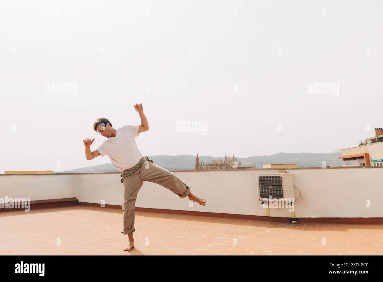 Unbeschwerter Mann, der auf einem Bein auf der Gebäudeterrasse vor klarem Himmel tanzt Stockfoto