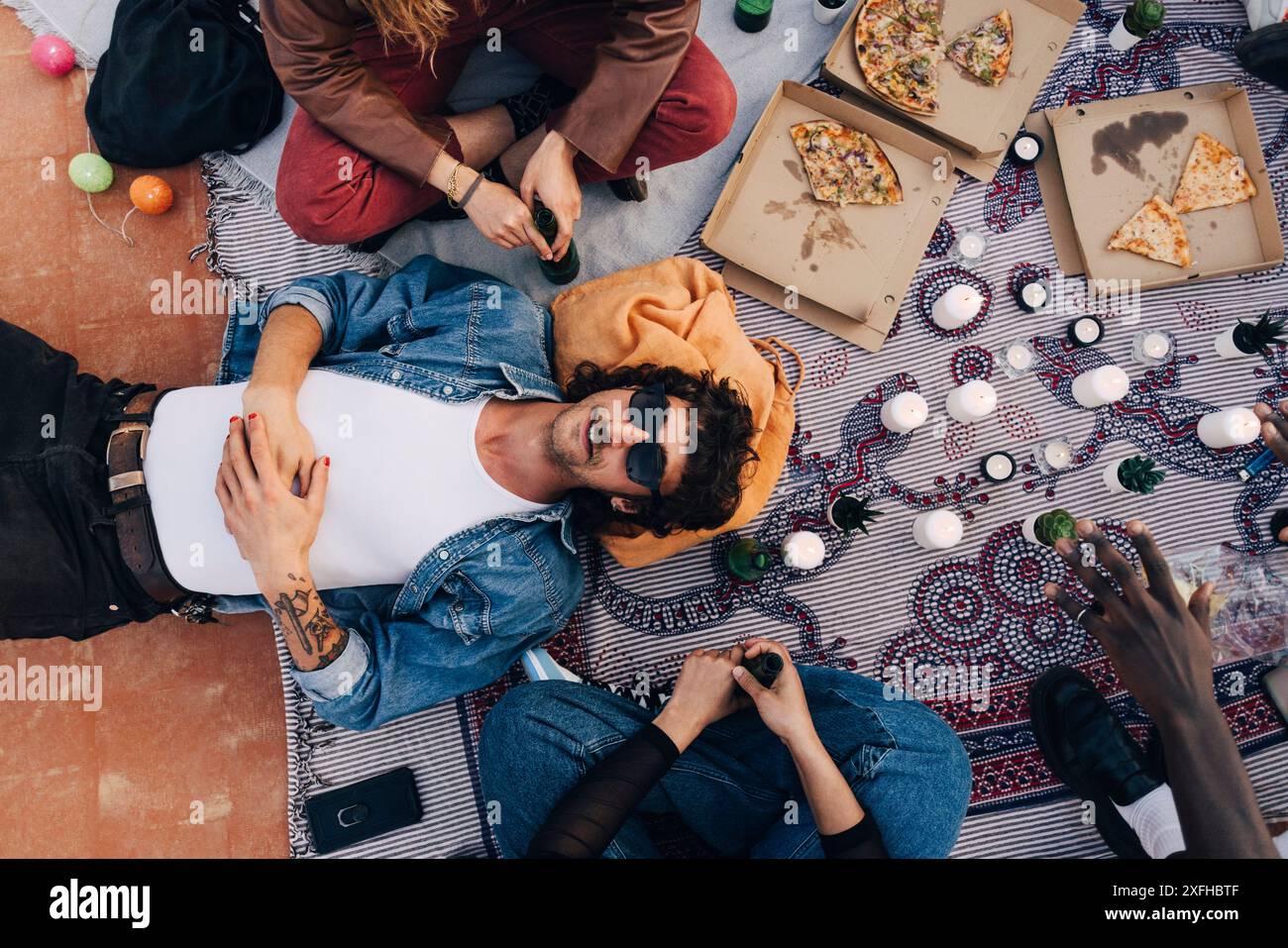 Direkt über dem Schuss eines Mannes, der von Freunden auf Picknickdecke während der Party liegt Stockfoto