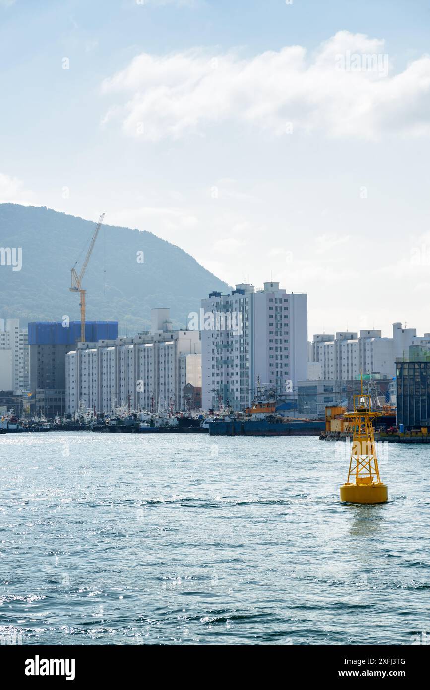 Gelbe Navigations-Boje am Hafen von Busan in Südkorea. Busan City ist auf blauem Himmel zu sehen. Malerische Stadtlandschaft. Stockfoto