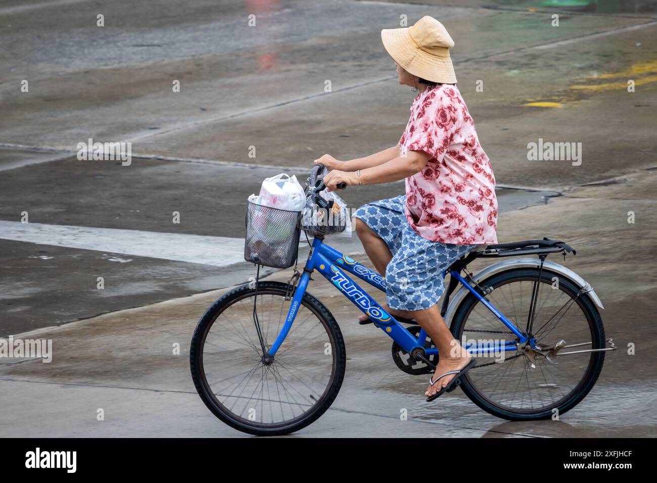 SAMUT PRAKAN, THAILAND, 21. MAI 2024, Eine Frau fährt Fahrrad auf einer nassen Straße Stockfoto