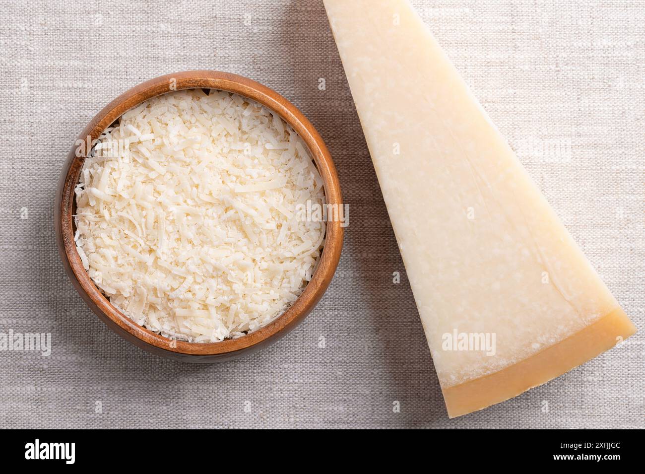 Geriebener Parmesankäse, Parmigiano Reggiano oder Grana Padano in einer Holzschale auf Leinen, mit dem ganzen Stück auf der rechten Seite. Italienischer Hartkäse mit Granulat. Stockfoto