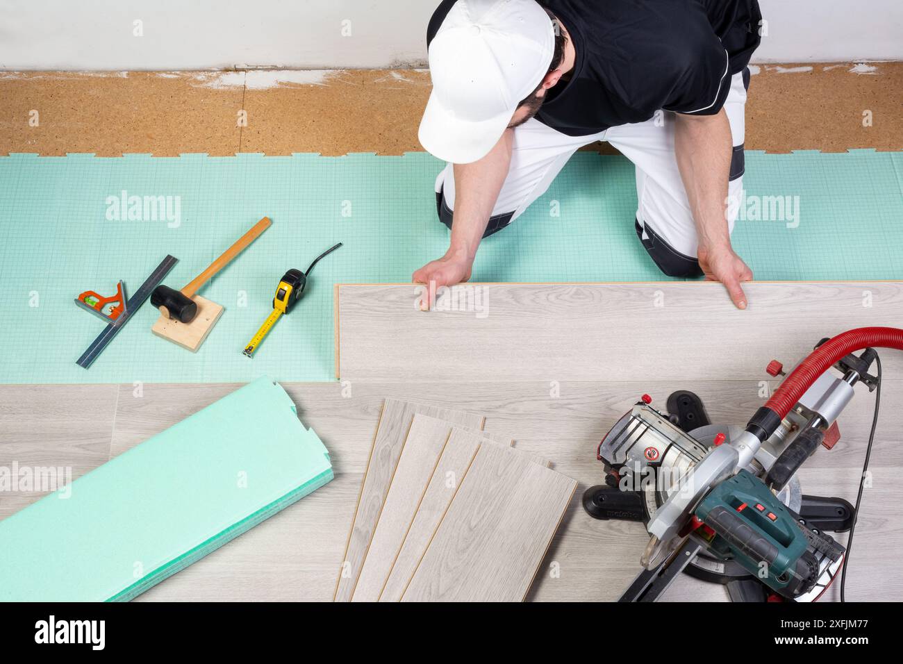 Männlicher Arbeiter, der Laminat- oder Vinylböden verlegt. Werkzeuge wie Hammerwalzen messen graue Laminatfliesen auf Trittschalldämmung. diy-Profi Stockfoto