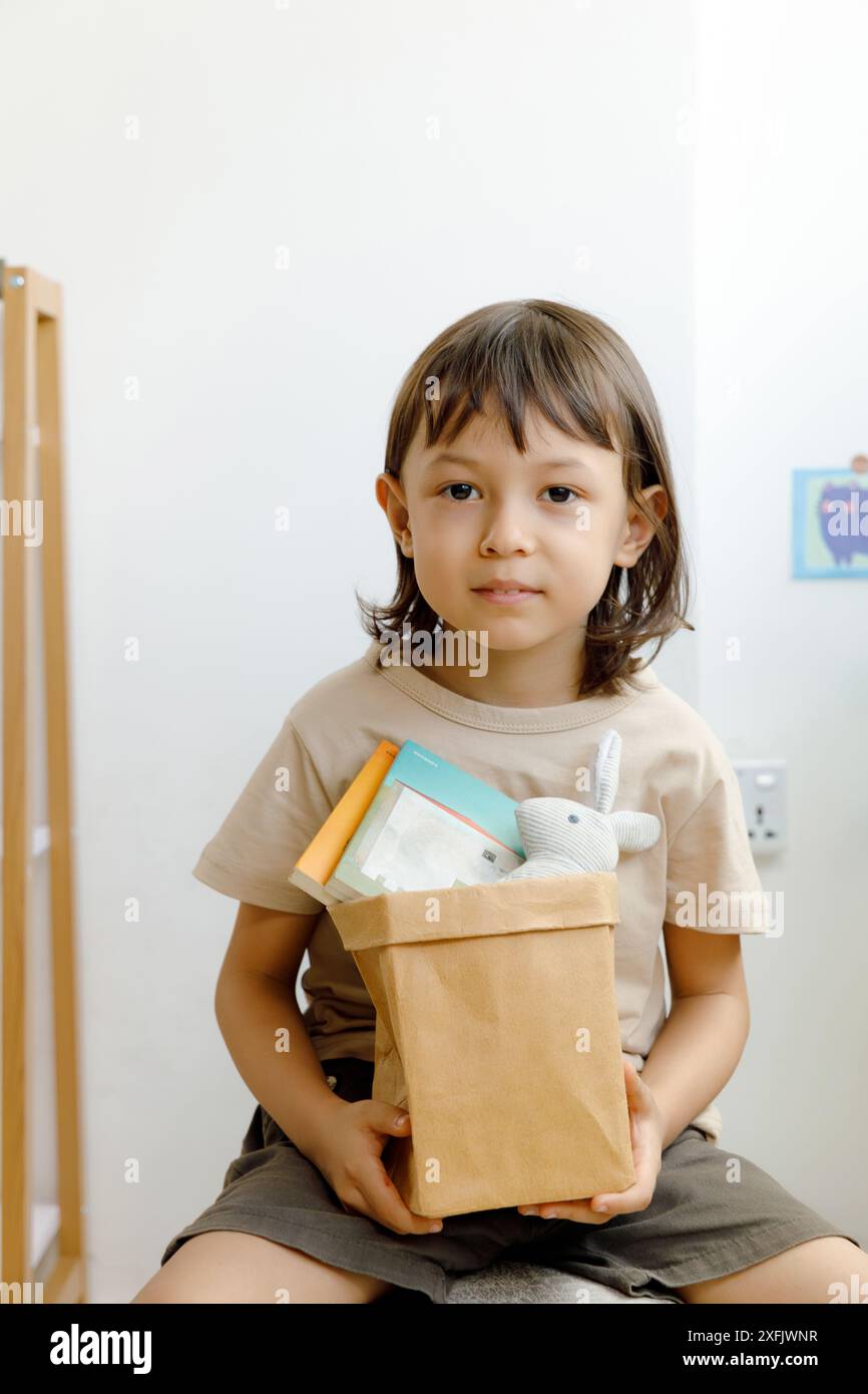 Ein nachdenklicher Junge mit einer braunen Papiertüte, der in einem einfachen Innenraum sitzt Stockfoto