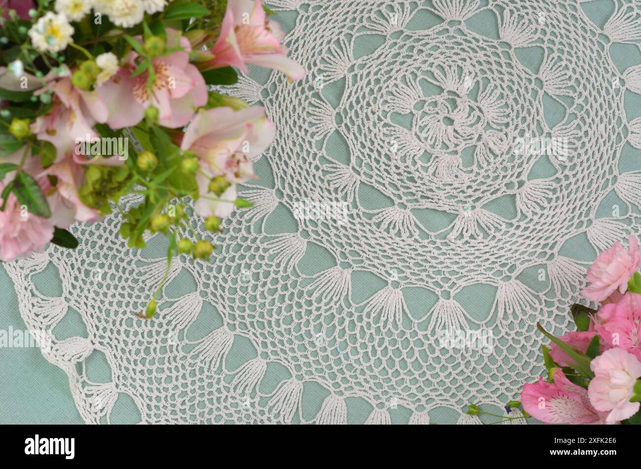 Weiße und mintfarbene Tischdecke, regionales Häkelmuster mit rosafarbenen Blumen. Geringe Schärfentiefe. Stockfoto