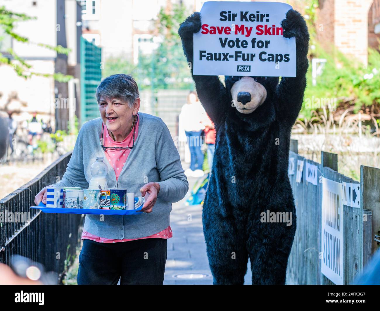 London, Großbritannien. Juli 2024. Eine nette Dame aus dem Wohnblock bringt ein Tablett Kaffee für die Presse raus und ignoriert einen PETA-Demonstranten, der als Bär verkleidet ist. Sir Keir Starmer trifft ein, um bei den Parlamentswahlen in seinem Wahllokal in Holborn und St Pancras zu wählen. Guy Bell/Alamy Live News Stockfoto