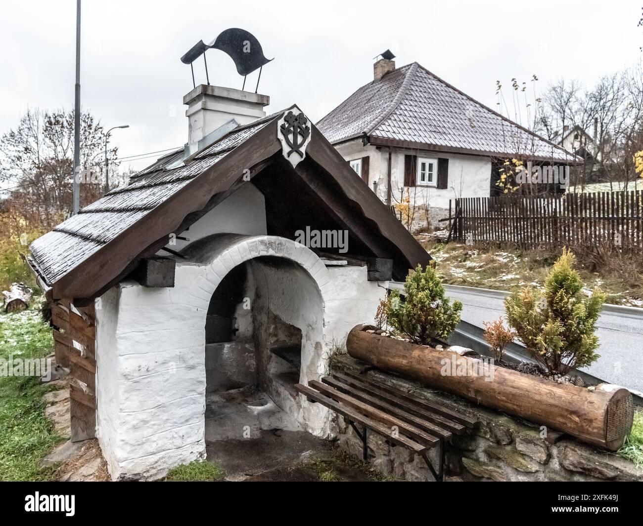 Ein Backofen aus dem 19. Jahrhundert in Lenora, Sumava, Tschechien. Mit weiß getünchter Struktur, Holzdach und bogenförmiger Öffnung. Umgeben von Bäumen und ländlichen Häusern. Stockfoto