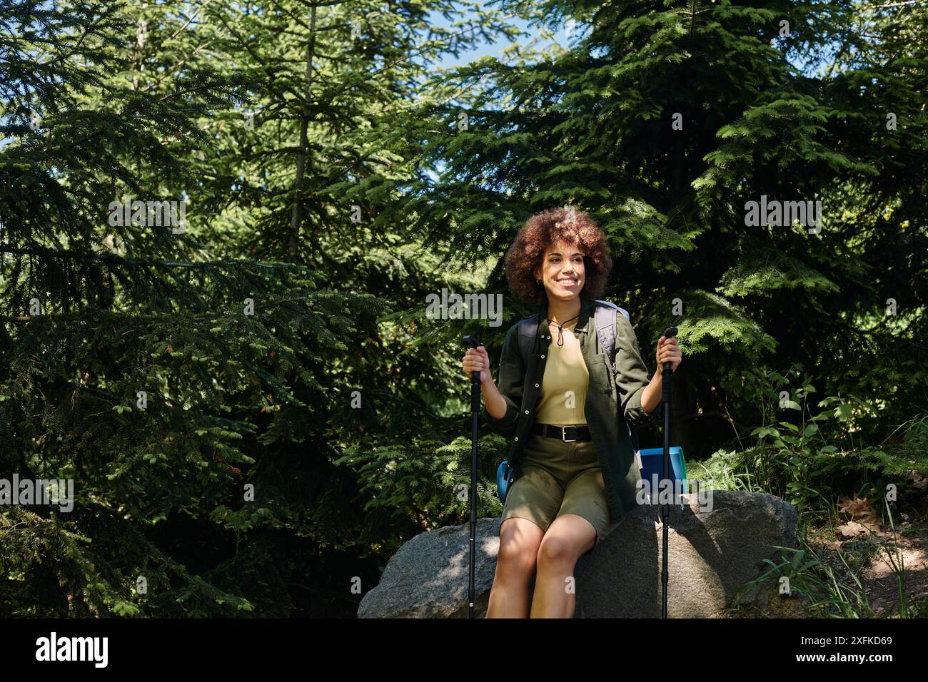 Eine junge Frau genießt während ihrer Wanderung eine Pause, sitzt auf einem Felsen in einem üppigen Wald, umgeben von hoch aufragenden Bäumen. Stockfoto