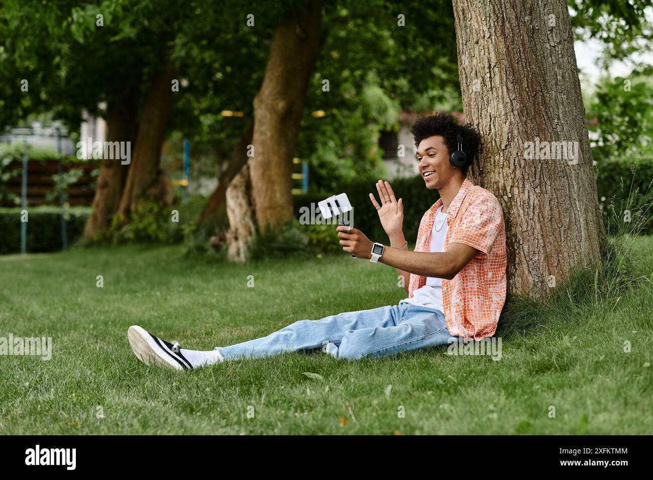 Junger afroamerikaner, der auf Gras sitzt, in der Musik verloren. Stockfoto