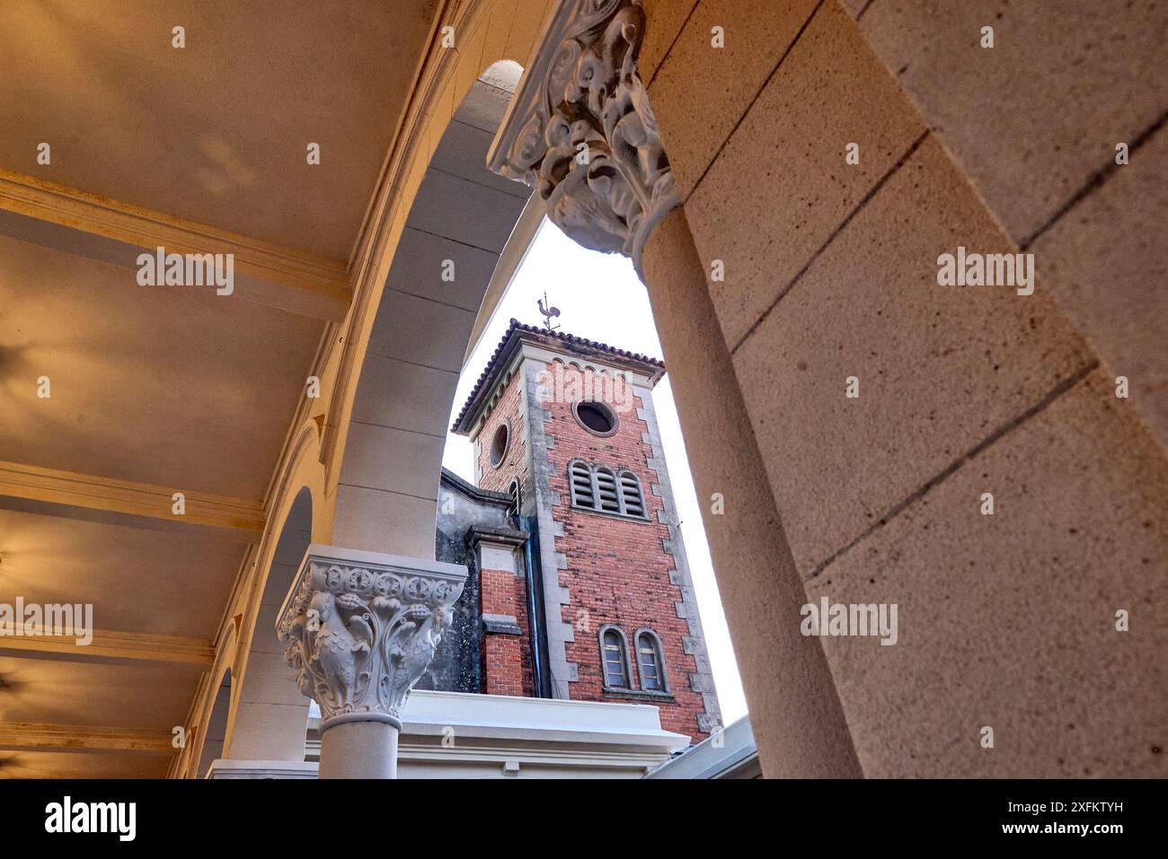 Blick auf den Glockenturm einer Abtei durch einen Bogen aus korinthischen Säulen. Oben auf dem Turm befindet sich eine schwarze Hahn Wetterfahne, kontrasti Stockfoto