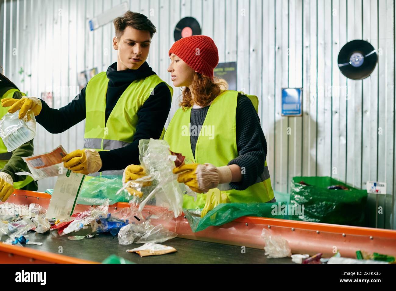 Junge Freiwillige in Handschuhen und Sicherheitswesten arbeiten zusammen, um Müll in einem Raum zu sortieren und ihr Umweltbewusstsein zu zeigen. Stockfoto