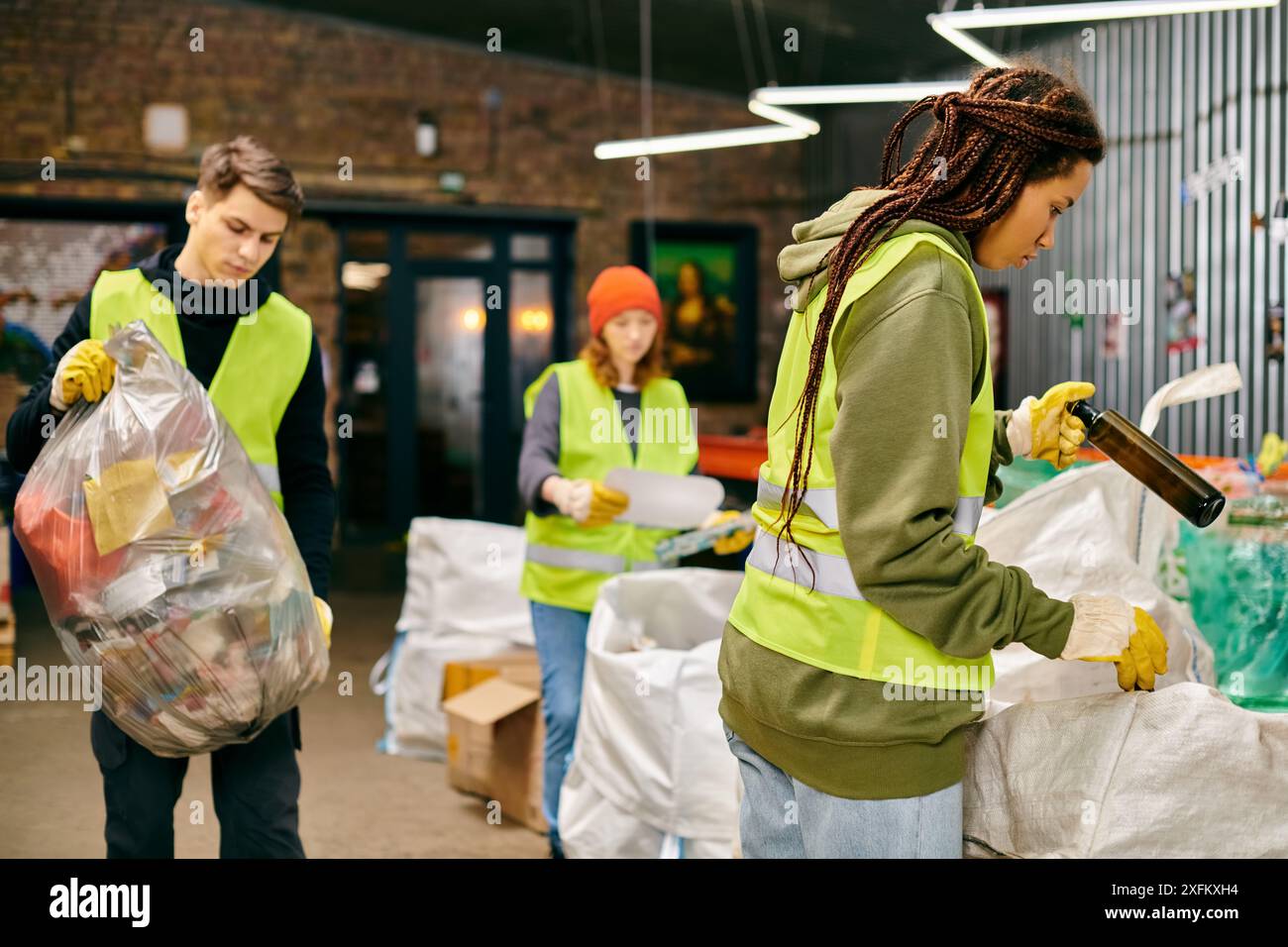 Junge Freiwillige in Handschuhen und Sicherheitswesten sortieren einen Müllhaufen, um das Umweltbewusstsein zu fördern. Stockfoto