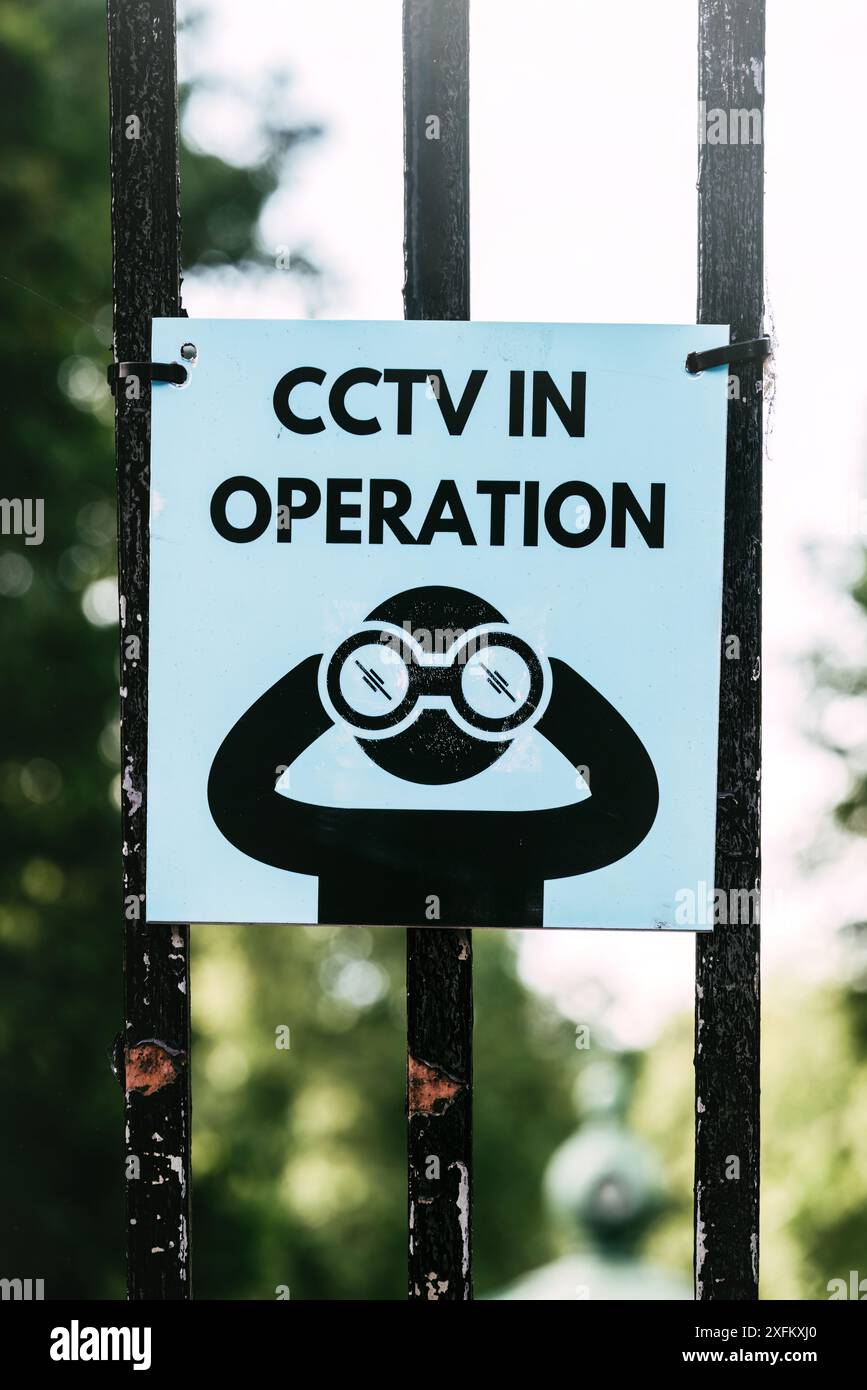 Ein blaues und schwarzes Schild mit den Worten CCTV in Betrieb und eine Cartoon-Person mit Fernglas, befestigt an einem schwarzen Metalltor in London Stockfoto