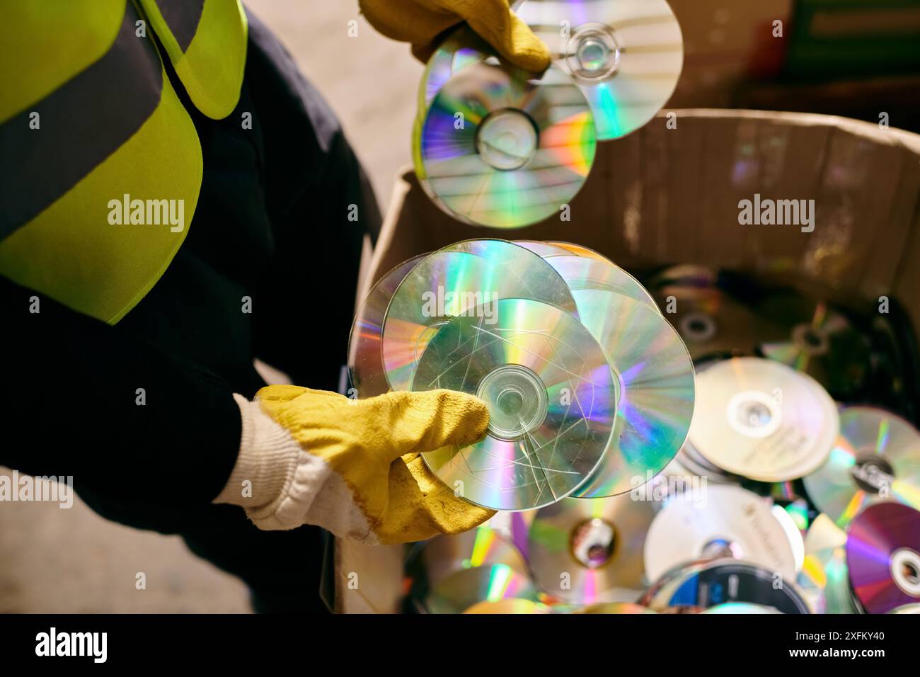 Ein junger Freiwilliger in Handschuhen und Sicherheitsweste, der einen Haufen CDs hält und Abfall im Rahmen umweltbewusster Bemühungen sortiert. Stockfoto