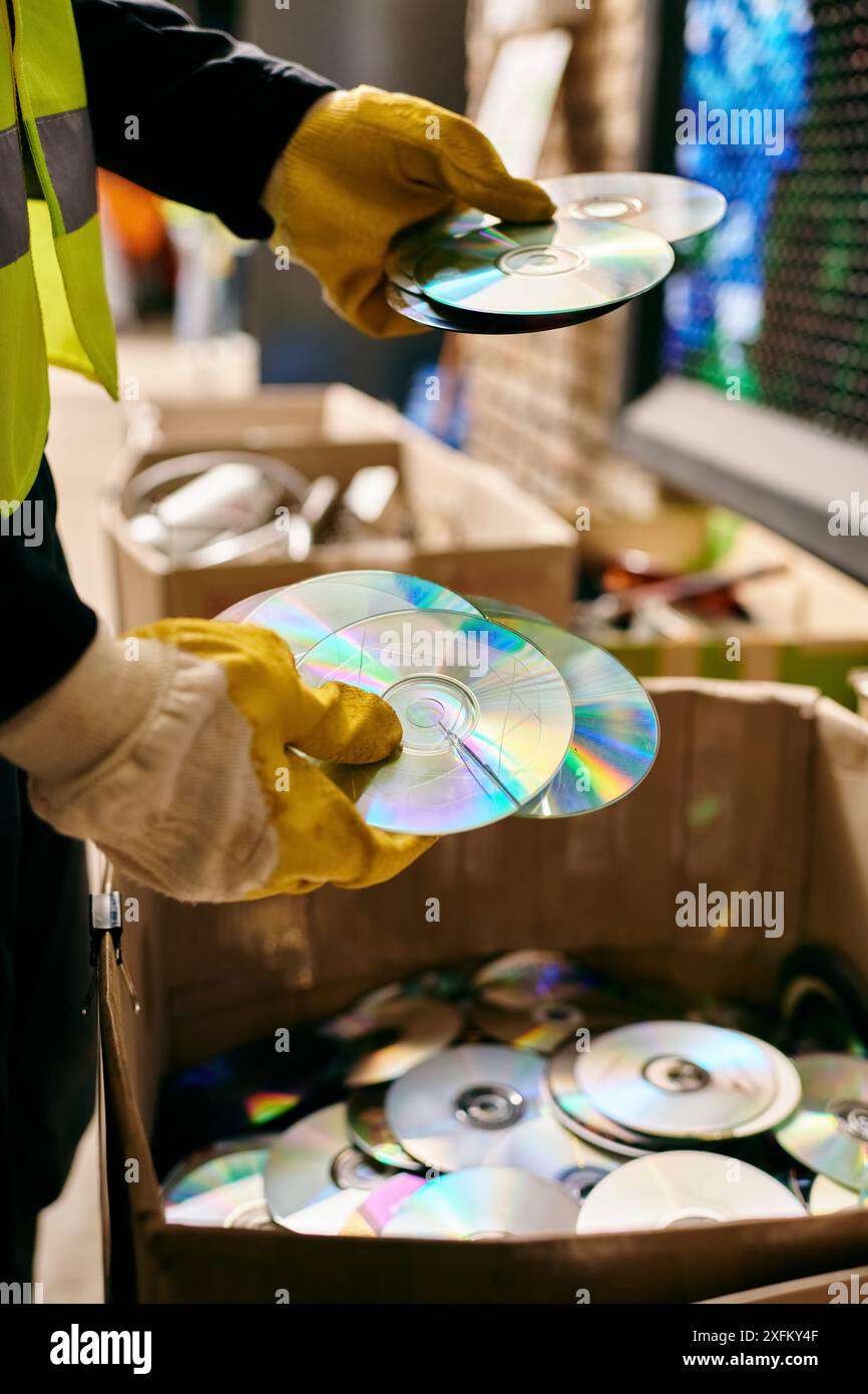 Junger Freiwilliger in gelber Sicherheitsweste hält beim Sortieren von Abfall vorsichtig eine CD und betont dabei umweltbewusstes Verhalten. Stockfoto