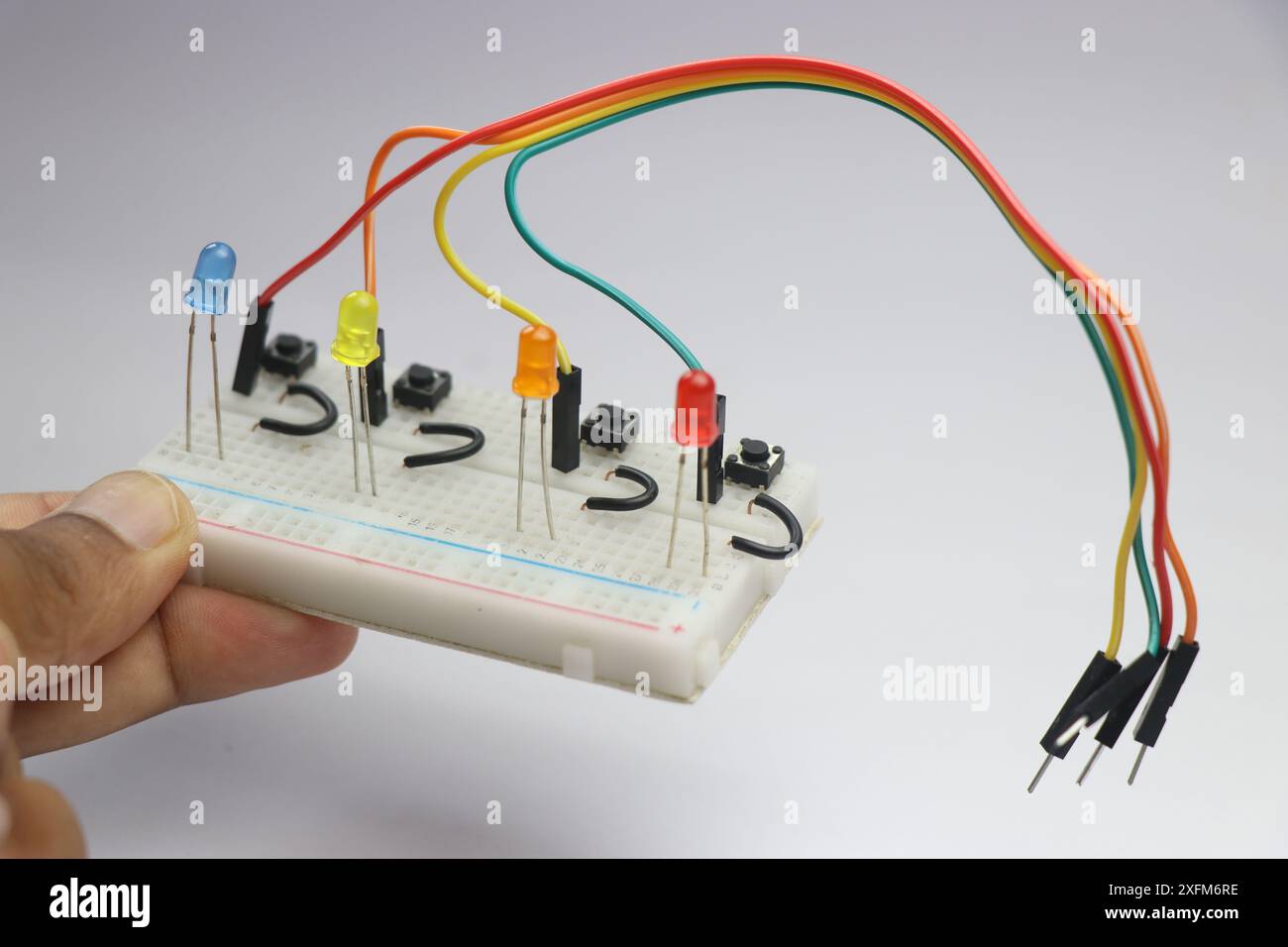 Kleine Steckplatine mit farbenfroher LED, die über Kabel und Überbrückungsdrähte mit einer in der Hand gehaltenen Kipptaste verbunden ist, die das Konzept der Erstellung veranschaulicht Stockfoto