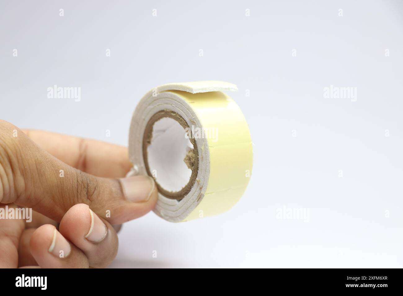 Zweiseitiges Klebeband oder auch als doppelseitiger Kleber bezeichnet, der auf weißem Hintergrund in der Hand gehalten wird Stockfoto