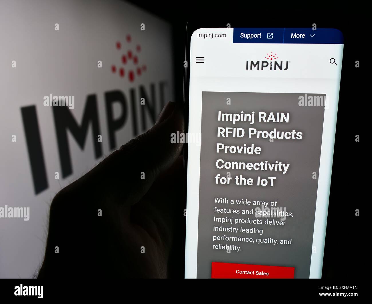 Person mit Smartphone und Website des US-RFID-Unternehmens Impinj Inc. Vor dem Firmenlogo. Konzentrieren Sie sich auf die Mitte des Telefondisplays. Stockfoto