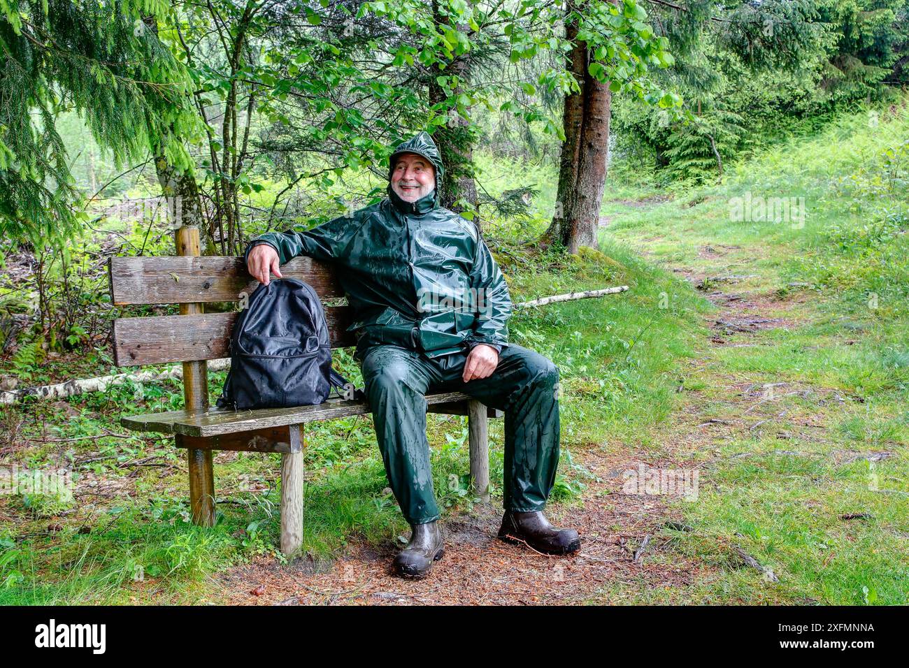 Auf dem Weg zur Kreuzbodenhütte macht ein älterer Wanderer eine Pause auf einer Bank entlang des Wanderweges und ist trotz des regnerischen Wetters gut gelaunt. Stockfoto