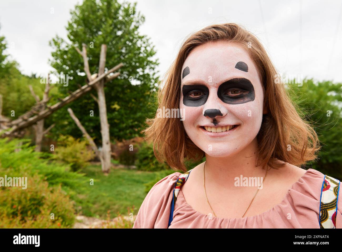 Teenager-Mädchen, das das Pandagehege im Zoo besucht, mit Pandaschminke. Beauval Zoo, Frankreich. August 2017. Modell freigegeben. Bitte kontaktieren Sie uns, um diese Bilder zu bestellen/zu lizenzieren. Stockfoto