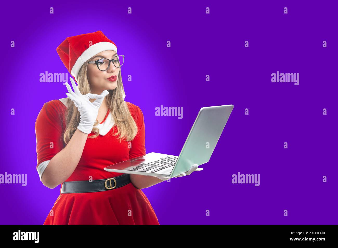 Junger Weihnachtsmann, der eine gute Geste macht, wenn er sich einen Inhalt auf einem Laptop ansieht, der auf violettem Hintergrund isoliert ist Stockfoto