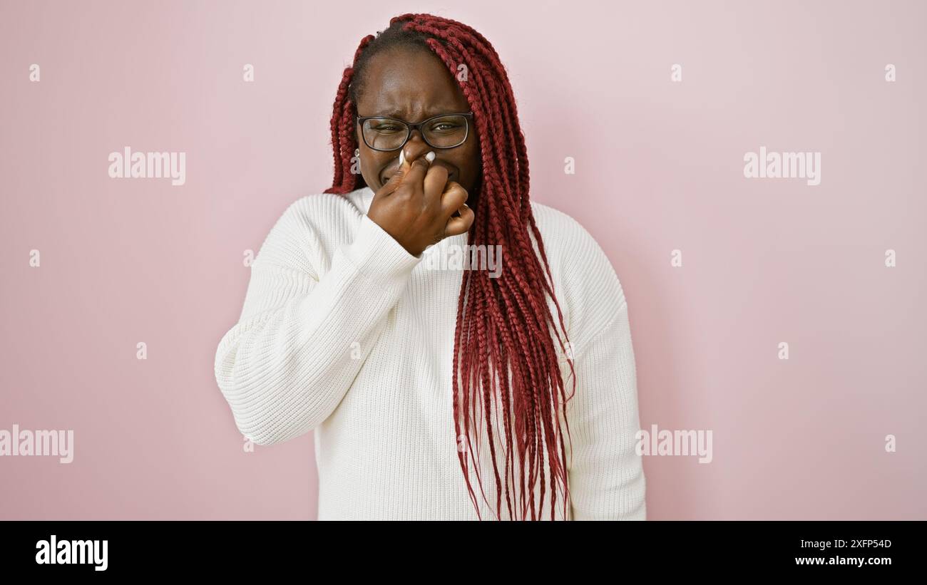 afroamerikanerin mit weißen Zöpfen auf rosafarbenem Hintergrund, die ihre Nase kneifen Stockfoto